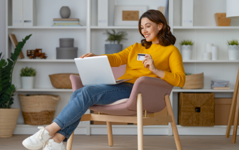 Smiling woman in a cozy home setting shopping online with a laptop and credit card, ideal for Amazon product videos.